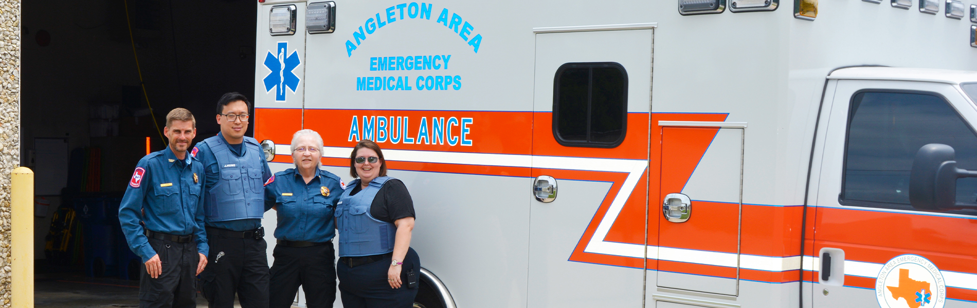image of four first responders wearing blue shirts and black pants standing in front of an ambulance
