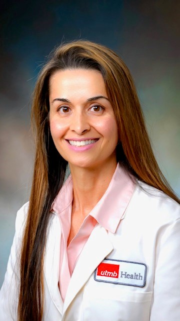 headshot image of smiling brunette woman with hair past her chest. she's wearing a pink collared shirt and a whitecoat 