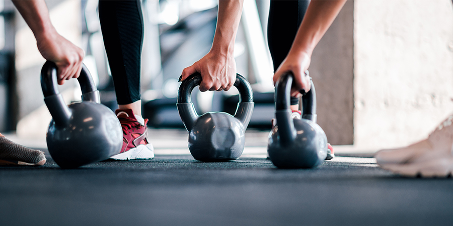 three kettlebells, each being grasped by hands while they rest on the floor