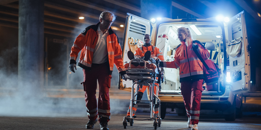 three paramedics, two male and one female wheeling patient out from ambulance