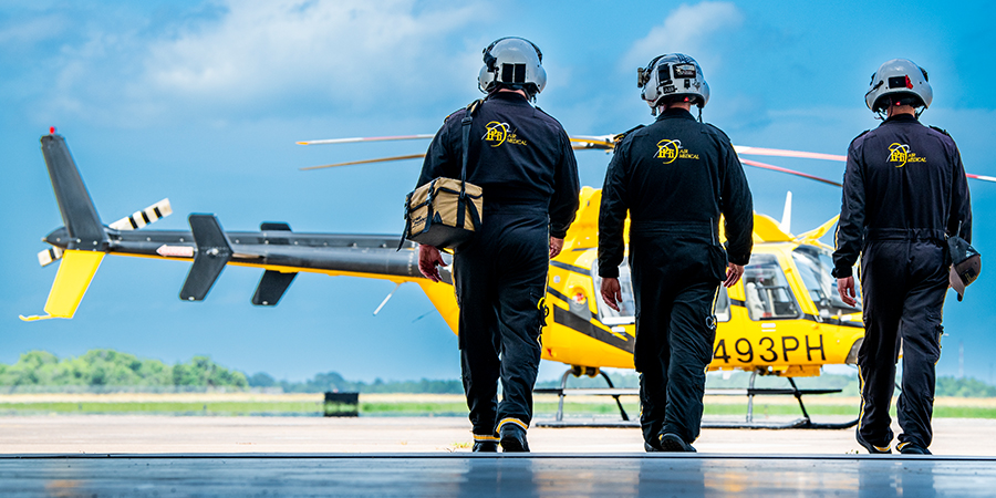 Three crew members with PHI Air Medical walk to a helicopter.