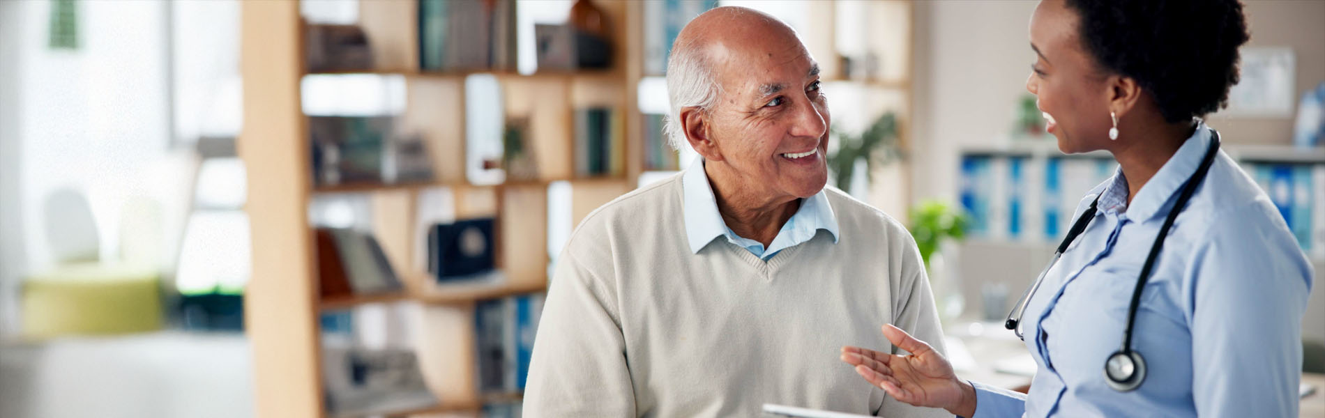 A patient smiles while talking with a doctor holding a tablet during a Medicare Wellness Visit.
