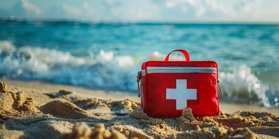 close shot at sand level of red first aid bag with white cross on it. waves are crashing in the background