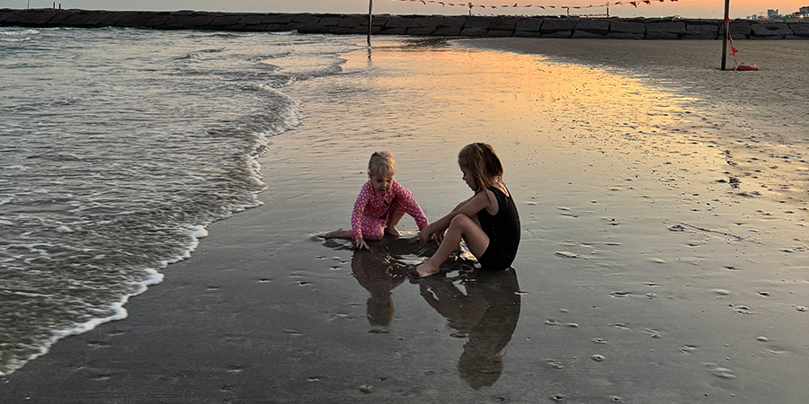 Two children play in the sand on the beach at sunset.