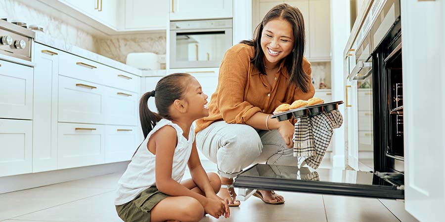 Daughter and mom taking muffins out of the oven