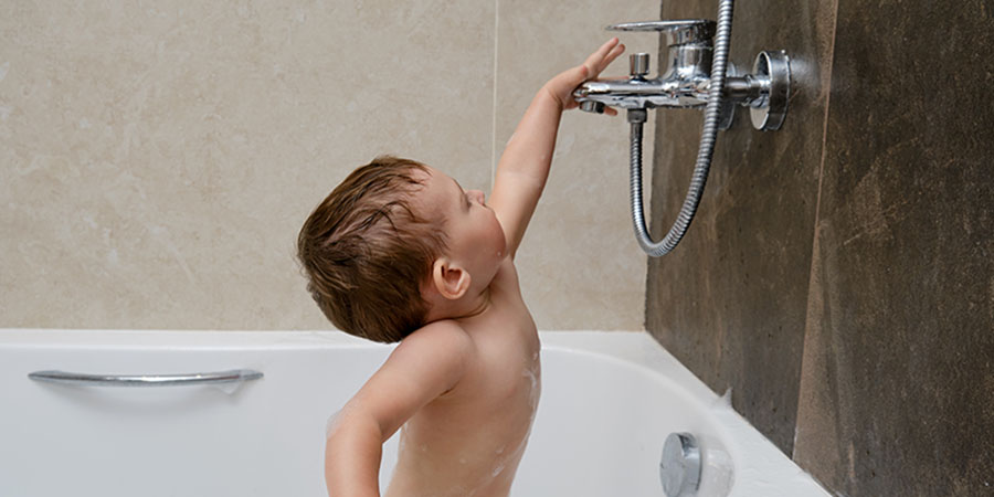 child in bath reaching for the faucet