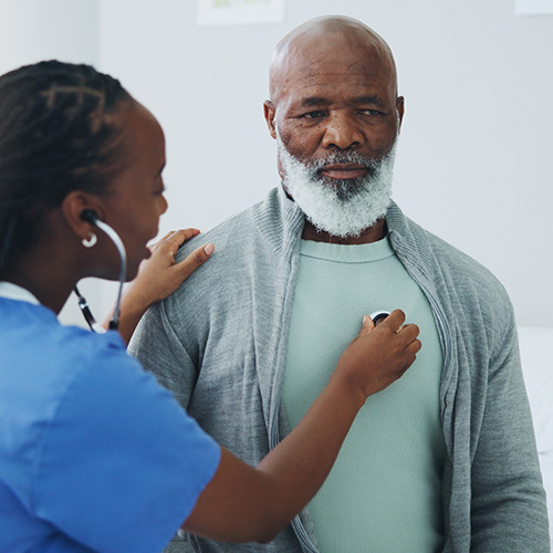 A health care worker listens to a middle aged man's heart with a stethoscope.
