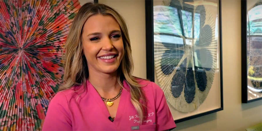 image of blonde-haired caucasian woman wearing pink scrubs and a gold heart necklace in front of framed fan art