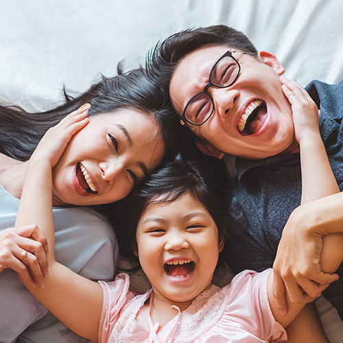 A family of three laying flat on a bed, happily embracing each other.