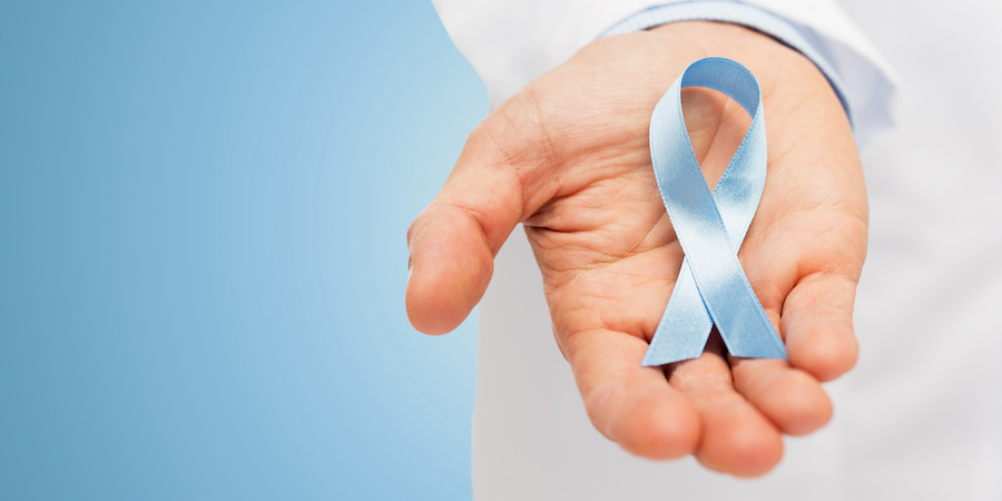 Close-up of a hand holding a light blue awareness ribbon against a blue background