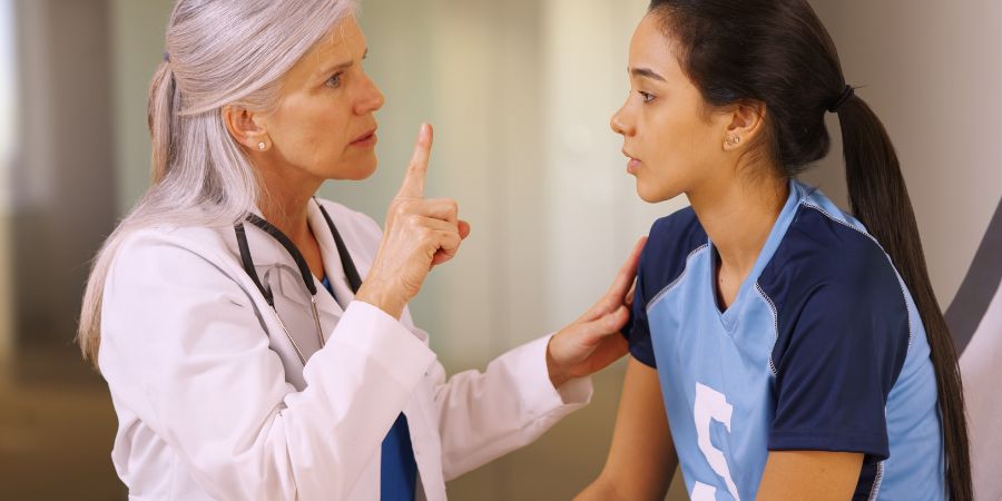middle aged caucasian female physician holding finger in front of the face of a young female athlete