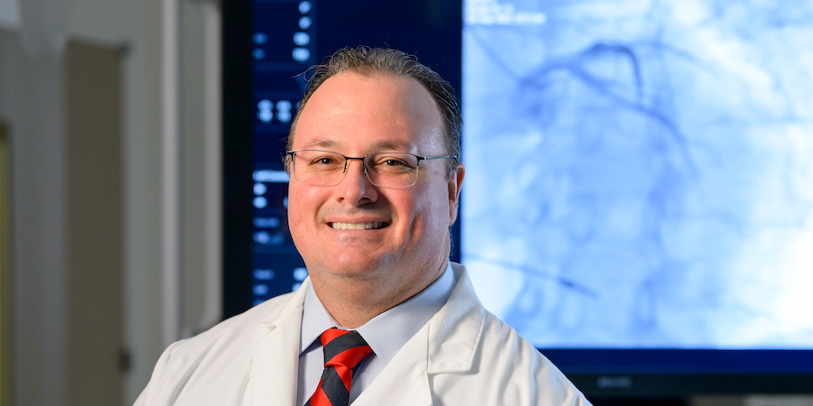 caucasian male physician wearing glasses, white coat and a navy and red striped tie standing in front of imaging screen