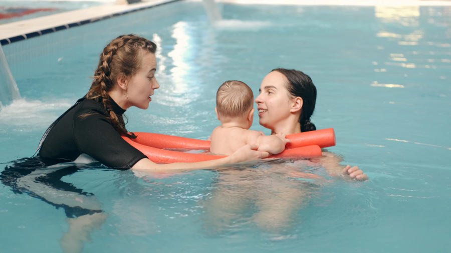 Image of female swim instructor with mother and infant in pool with red pool noodle