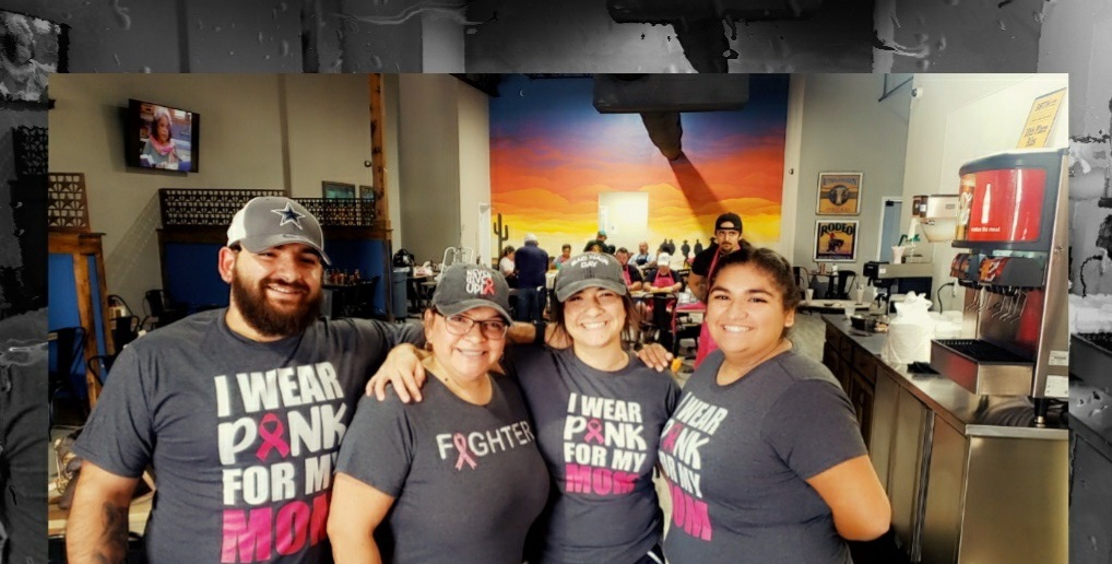 one male and three women posing, smiling for photo, each wearing gray hats and shirts with pink ribbons and words in support of breast cancer awareness 