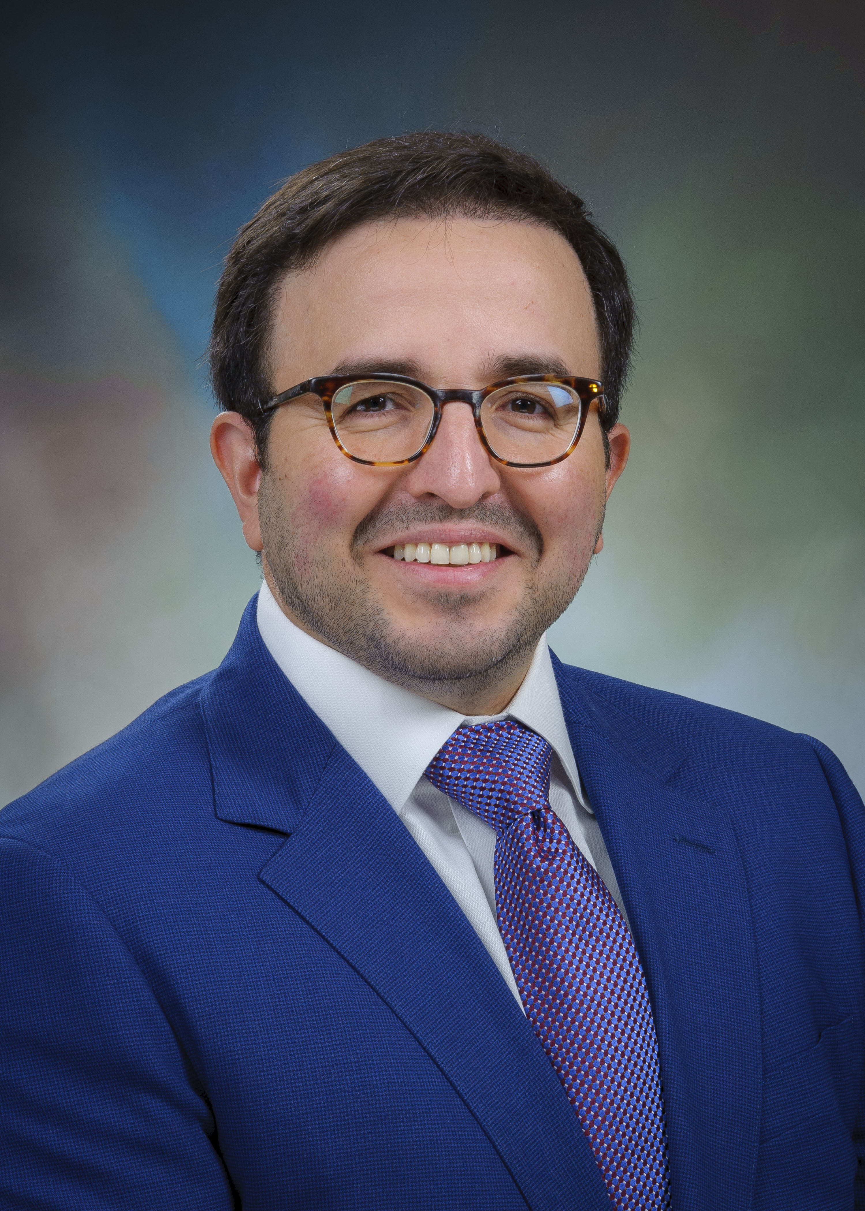headshot image of male physician wearing a blue blazer, glasses and a tie