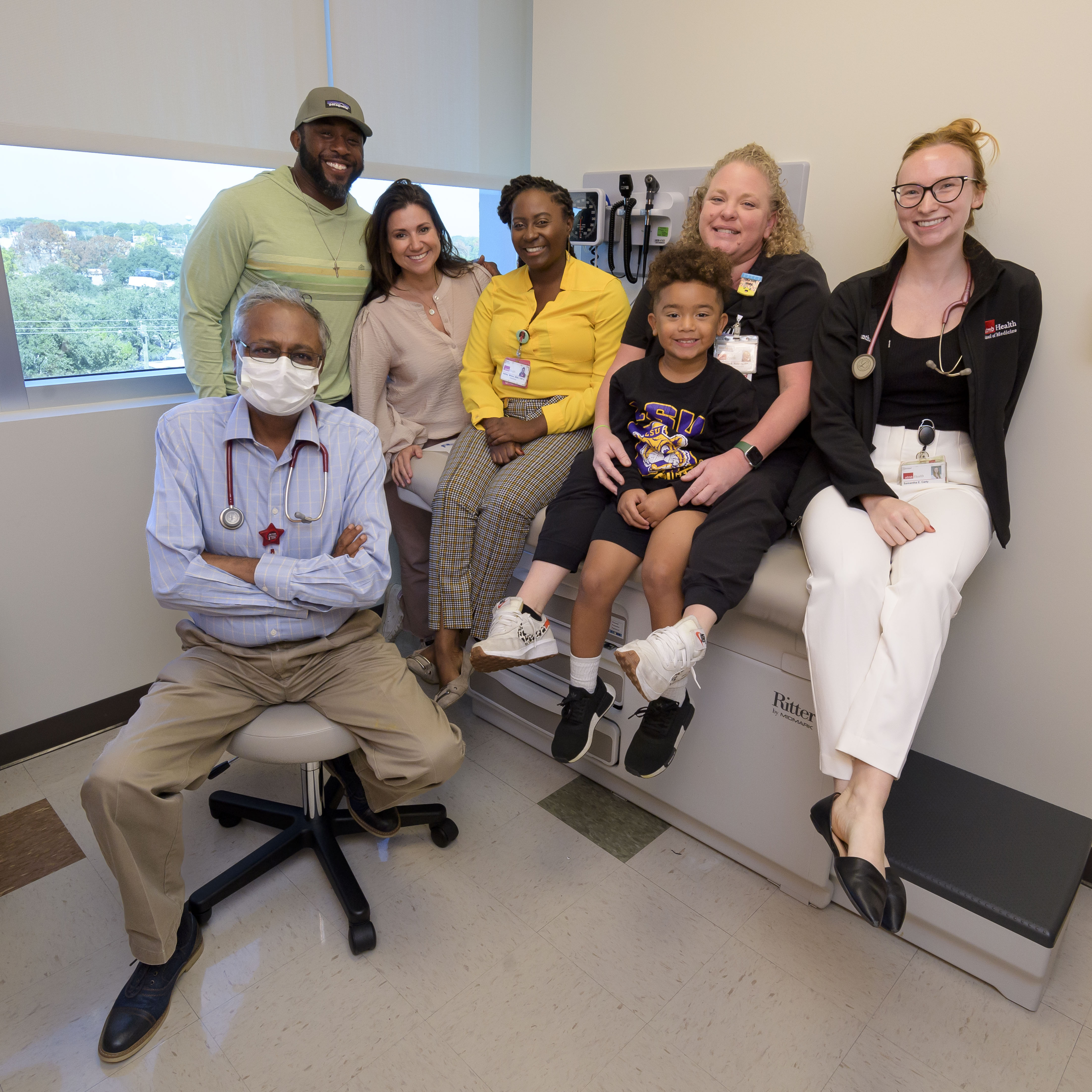 group of 6 adults sitting and standing around male pediatric patient in a clinic setting