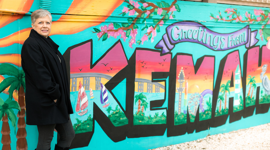 image of female UTMB Health patient wearing all black and standing by "Greetings from Kemah" sign