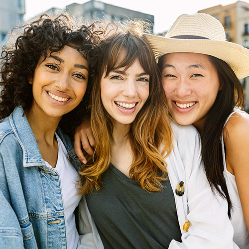 Three diverse women stand and smile together.