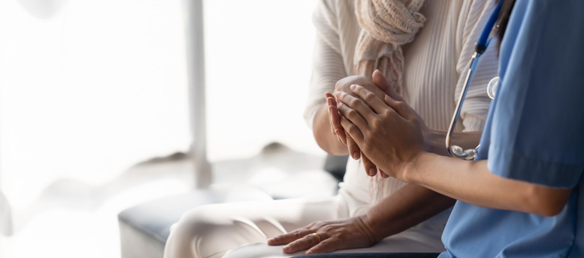 A healthcare provider gently holds a patient's hands, offering comfort and support during care.