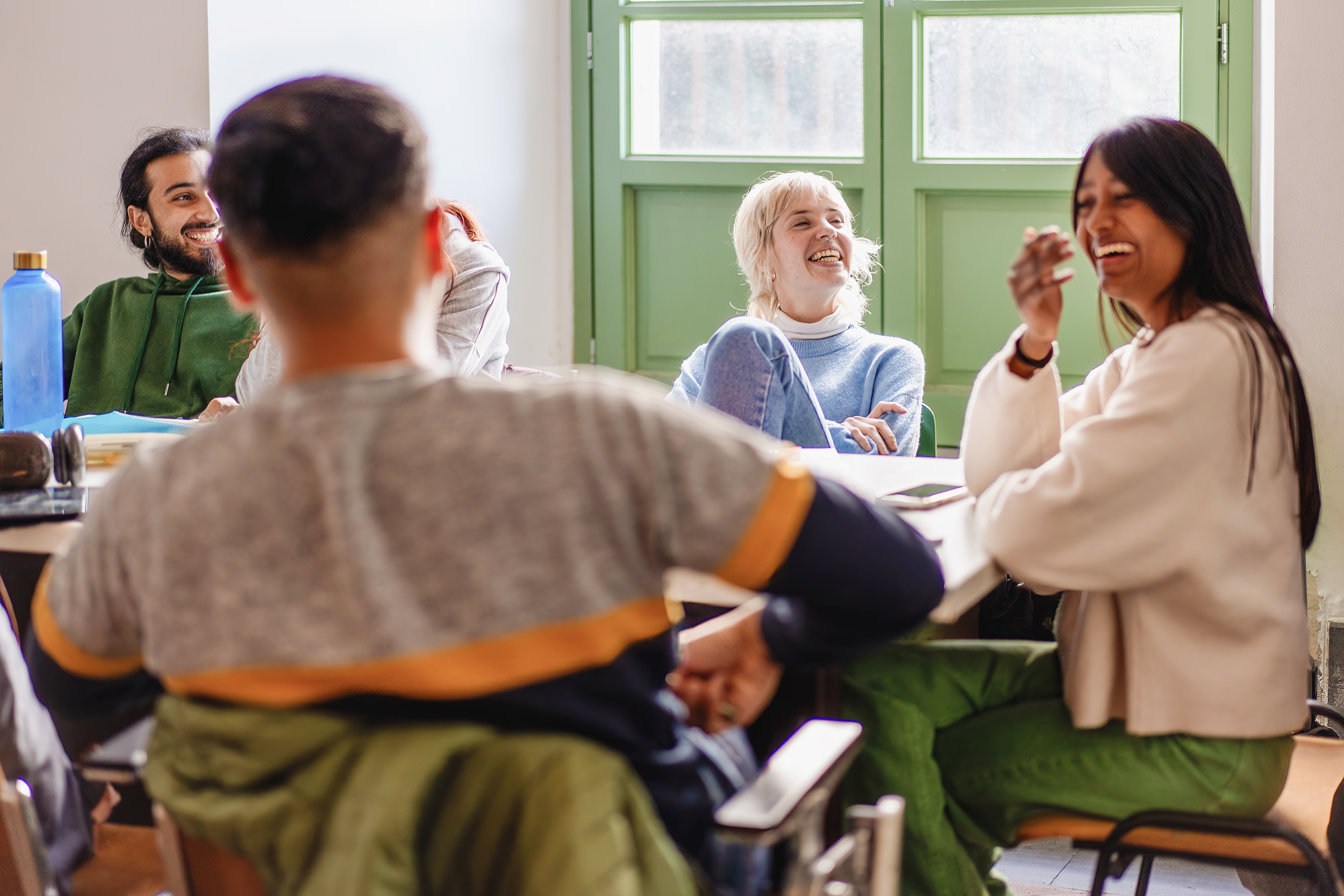 A diverse group of young adults sit together and laugh during a community education session.