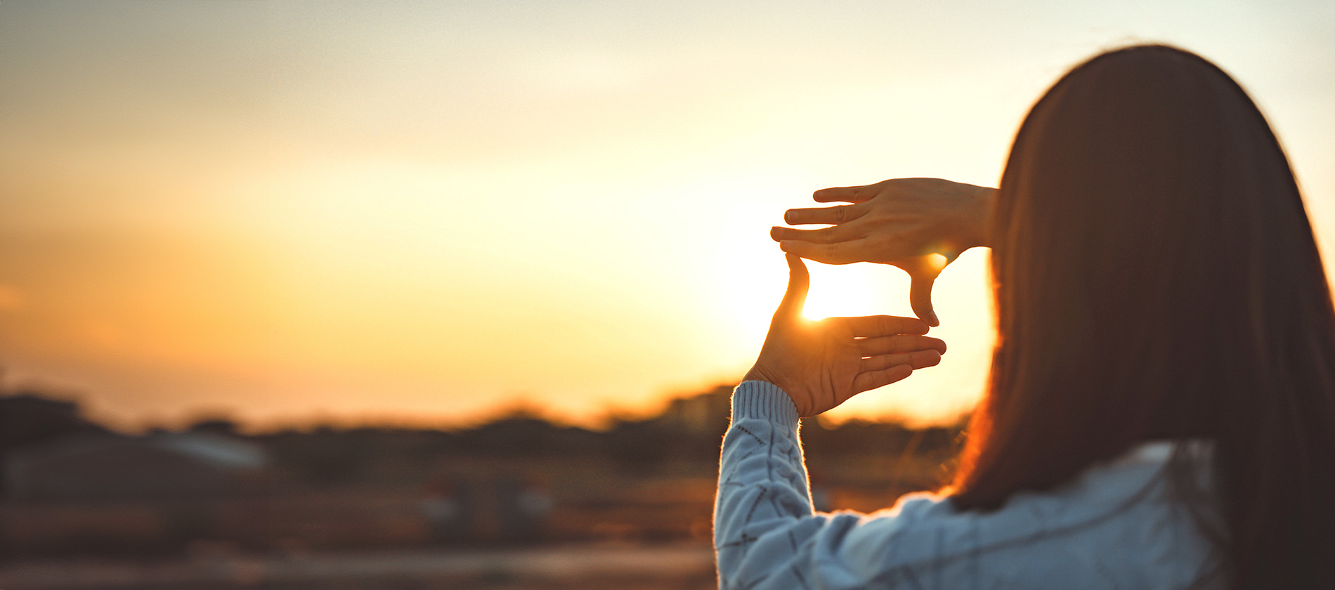 A person frames the sun with their hands, symbolizing clear vision and a high quality of life after eye care.