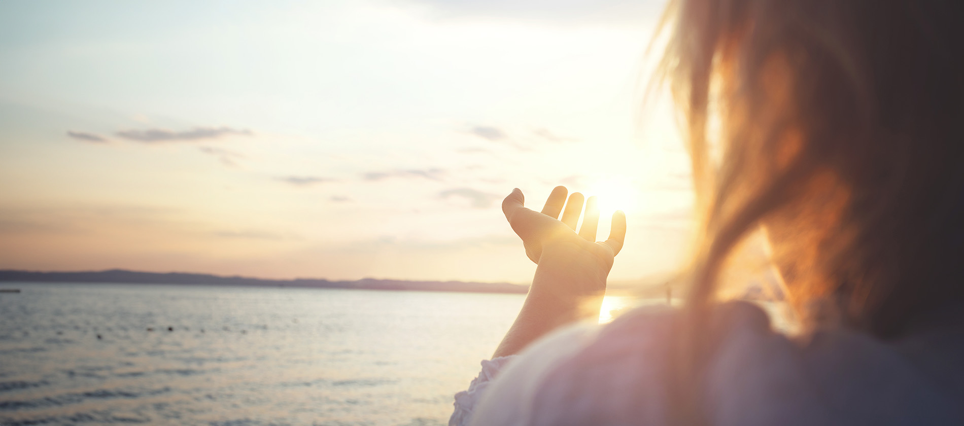 A person reaches toward the setting sun over the water, symbolizing hope and healing