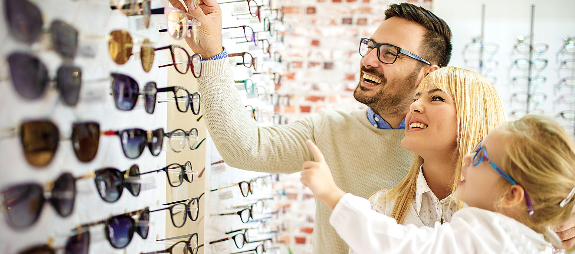A smiling family browses a wall of eyeglass frames at a UTMB Optical Center.