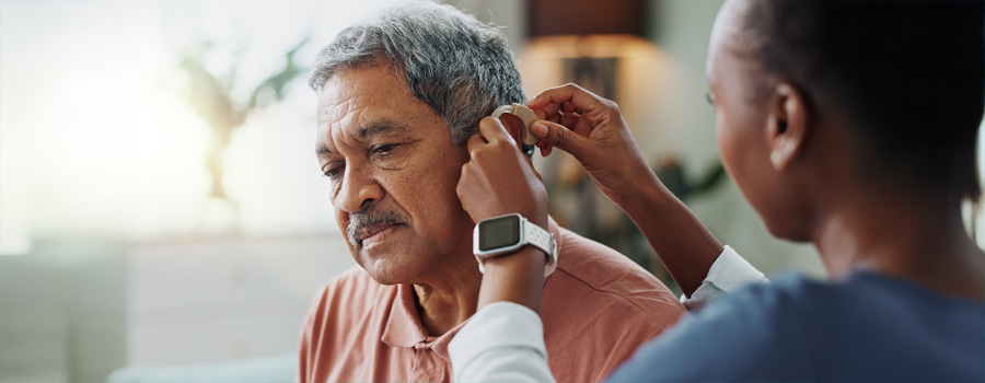 A healthcare professional helps an older man adjust his hearing aid during treatment for hearing loss.