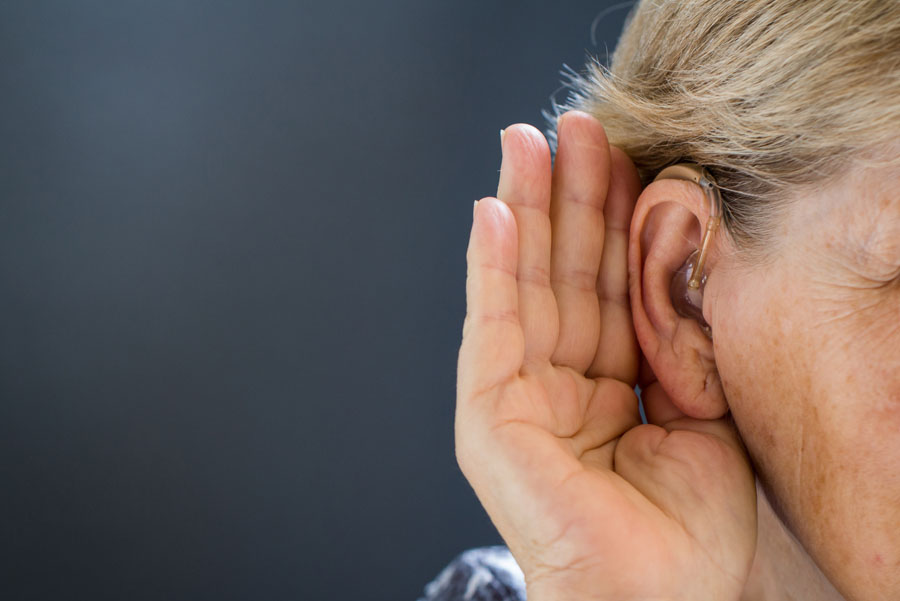 Women holding hand near ear wearing a hearing aid