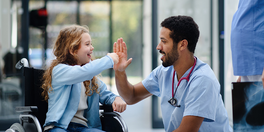Young multiracial doctor having fun with little girl on wheelchair.