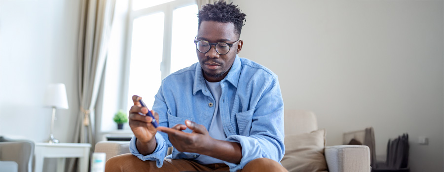 Man with diabetes sitting on sofa while taking blood from his finger to test his glucose.