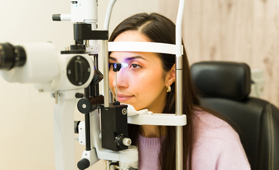 Seated young woman getting professional eye exam with a slit lamp by an ophthalmologist, checking vision