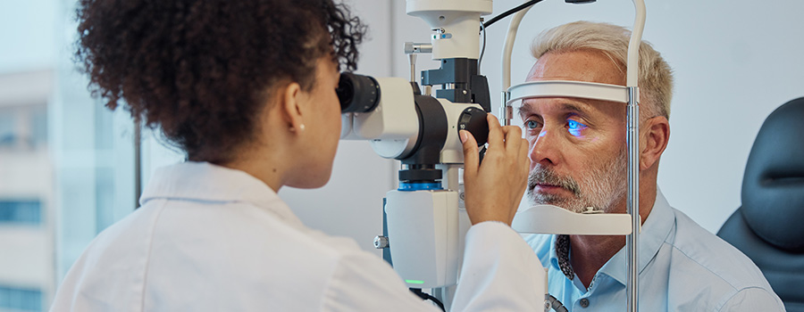 An eye care specialist performs a cataract screening on an older male patient using a slit lamp.