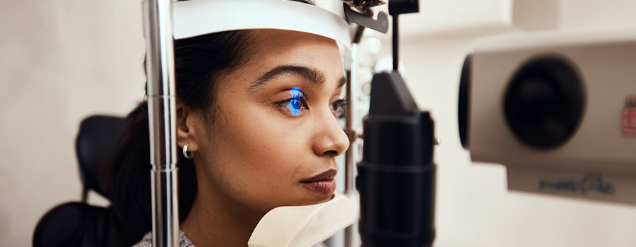 A woman undergoes an eye examination using a blue light scan to check for medical eye conditions. 