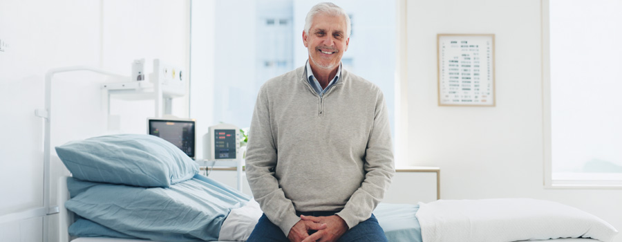 Smiling man sitting on hospital bed after colorectal procedure