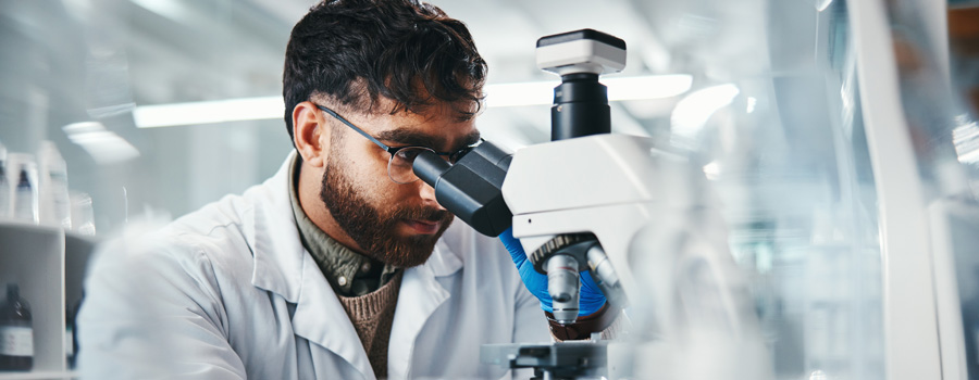 A genetics researcher studies DNA samples under a microscope while analyzing hereditary cancer risk testing at UTMB Health.