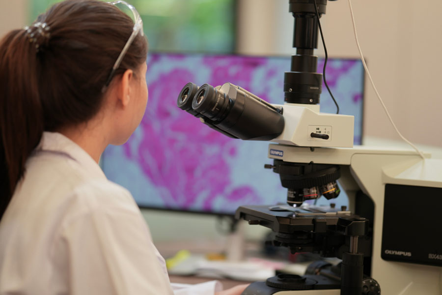 A laboratory scientist studies genetic samples under a microscope while analyzing DNA and genetic testing results at UTMB Health.