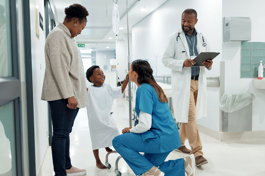A genetics specialist kneels to speak with a young patient and family during a medical genetics consultation at UTMB Health.