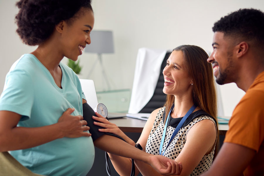 A clinician checks blood pressure while speaking with a pregnant patient and partner during a prenatal genetics visit at UTMB Health.