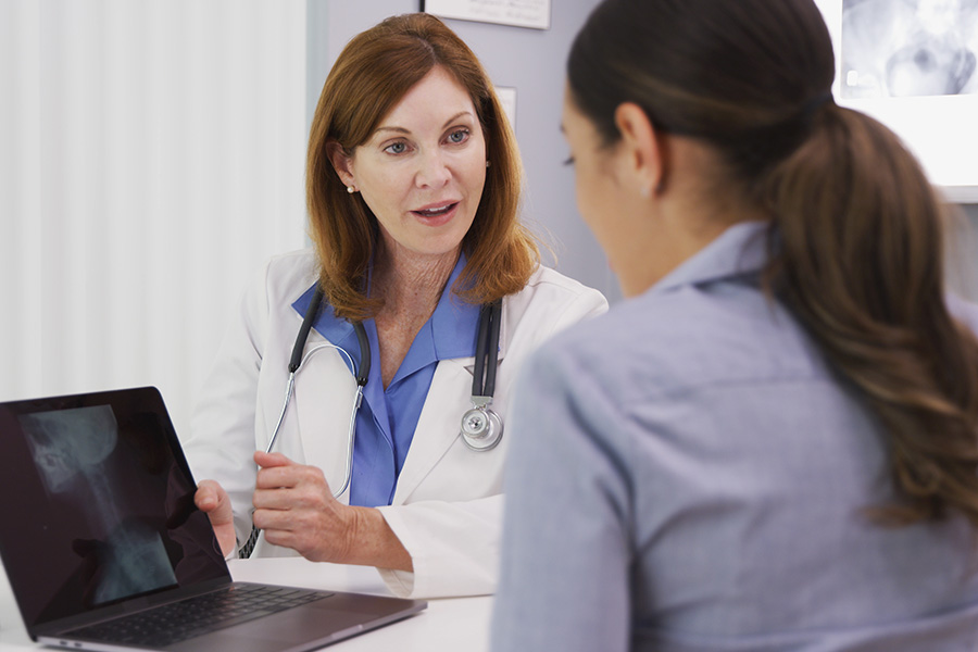 A doctor in a white coat discusses scan results with a patient, showing images on a laptop. This represents UTMB’s expert and compassionate approach to diagnosing and treating head and neck cancers. 