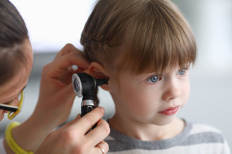 A healthcare provider examines a young child's ear with an otoscope, checking for signs of infection or hearing issues. This represents UTMB’s specialized pediatric head and neck care. 