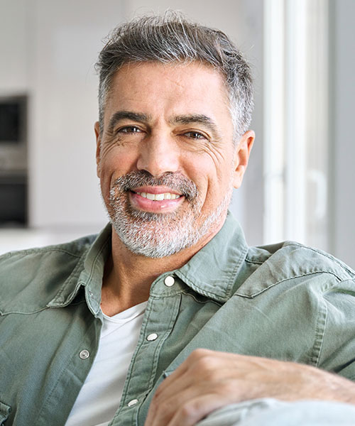 Portrait of happy smiling middle aged mature senior 50 years old bearded man wearing green shirt sitting on couch