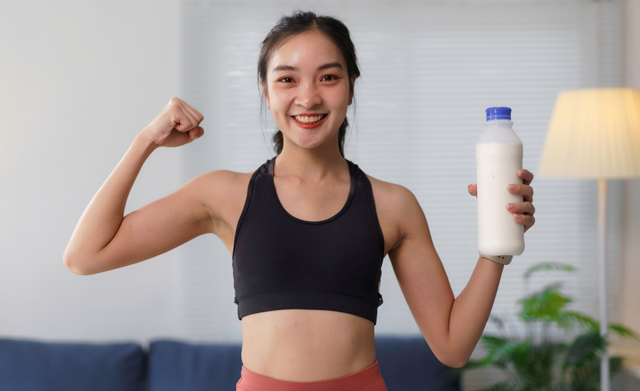 Smiling young woman flexing her bicep and holding a bottle of milk, promoting healthy lifestyle and calcium intake for strong bones