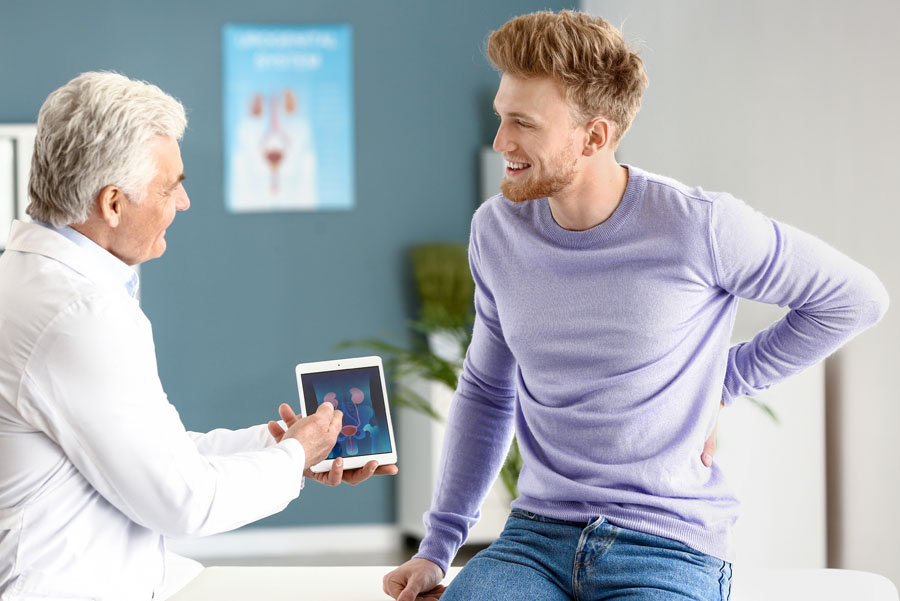 A doctor uses a tablet to explain kidney-related results to a smiling young adult patient.