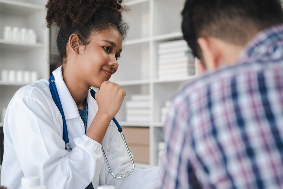 A young female provider speaks kindly to a seated patient during a kidney transplant follow-up visit.