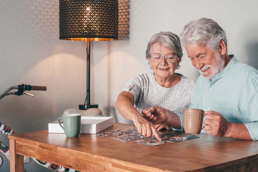 An older couple works together on a jigsaw puzzle while enjoying coffee at home.