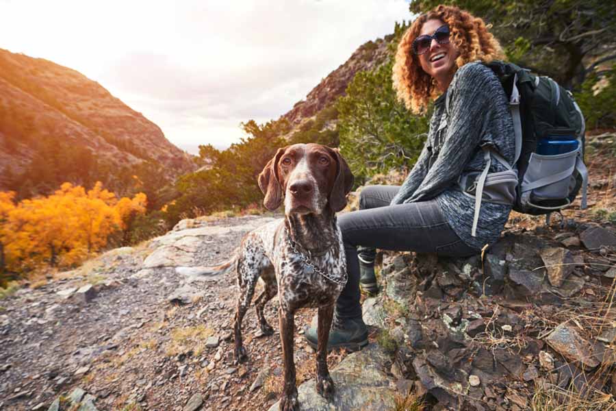 A woman sits on a rocky trail with her dog during a hike showing balance confidence and an active lifestyle.