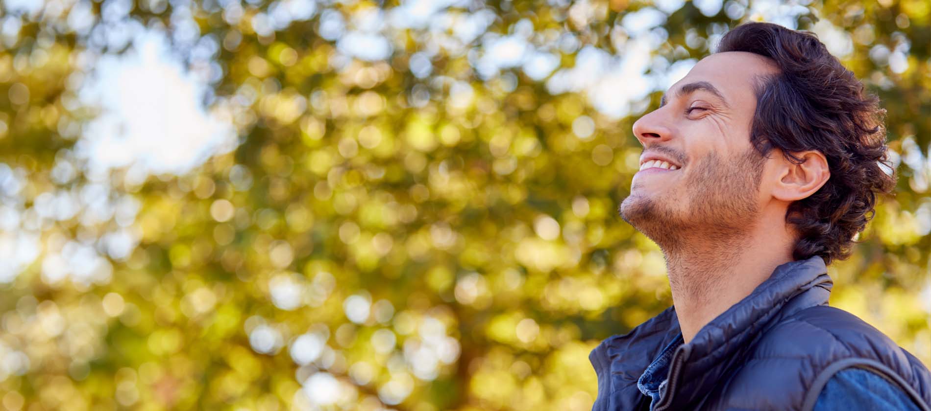 An adult stands outdoors with eyes closed and a calm expression suggesting relief comfort and wellbeing.