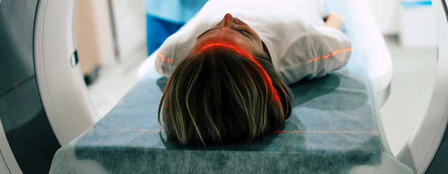 A patient lies still during a brain imaging scan while a healthcare professional monitors the procedure.