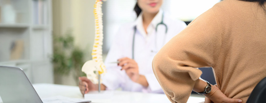 A patient discusses back and nerve symptoms with a provider using a spine model during evaluation for chronic pain and spasticity.